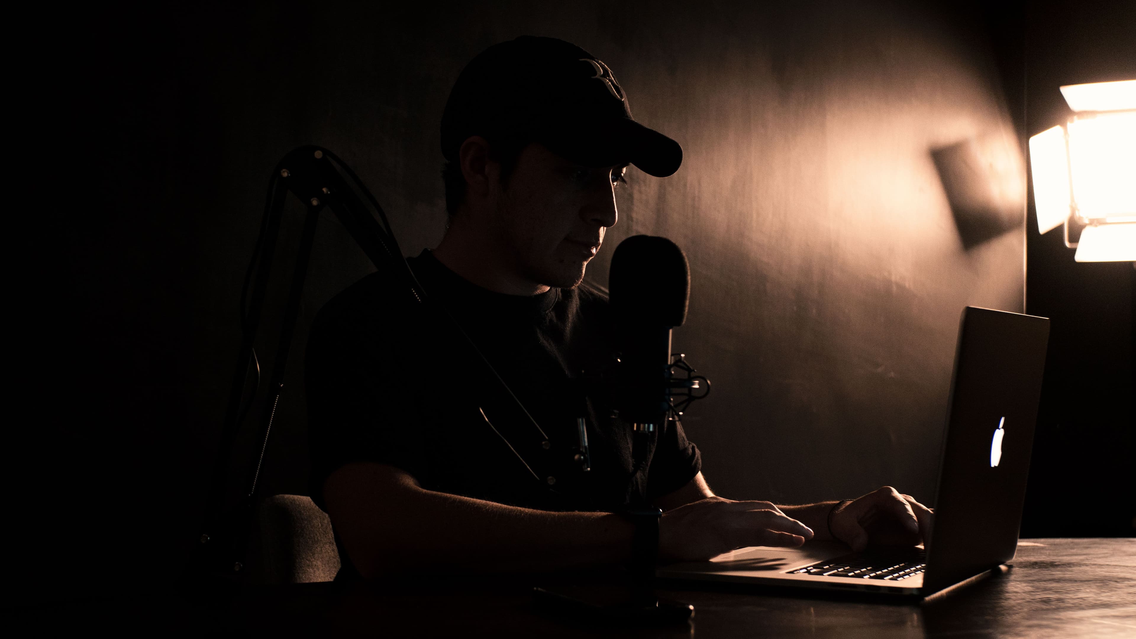 Creator working at a laptop with microphone setup in a dim workspace.