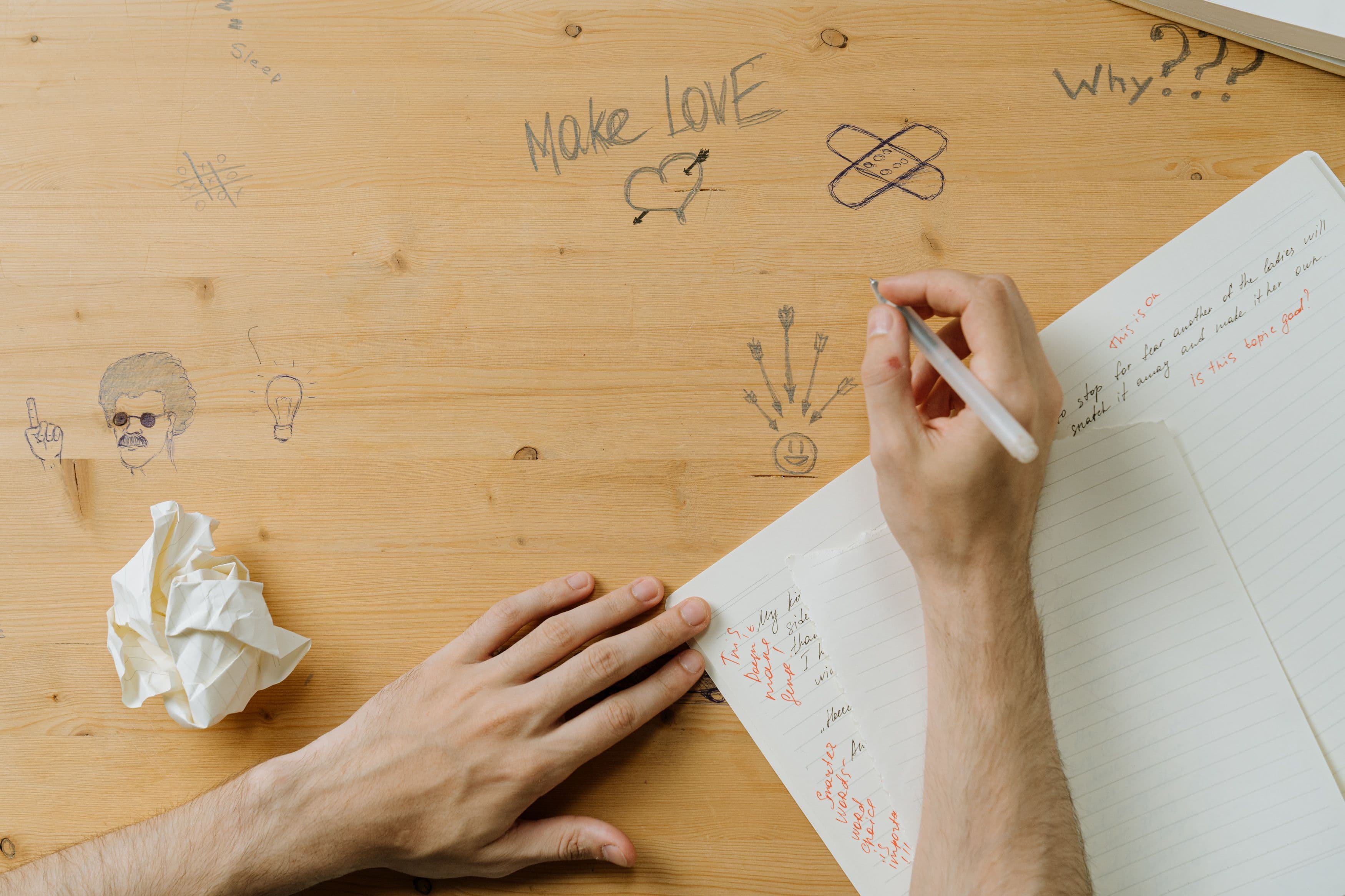 Person writing notes and sketches across a creative desk surface.